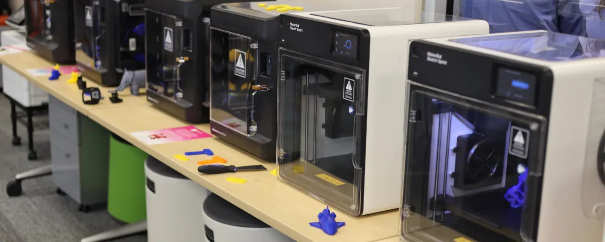 Several 3D printers on a table in a STEM classroom.