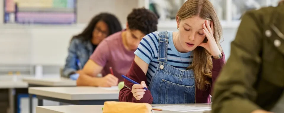Student feeling stressed while taking a test on paper in a classroom.