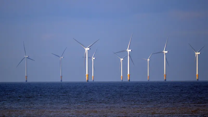 A group of offshore wind turbines standing in the ocean.