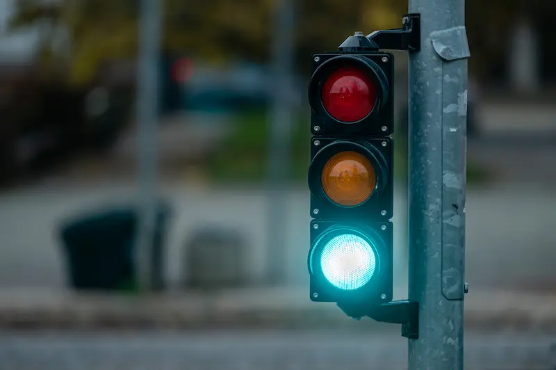 A traffic light in a city with red, yellow, and green lights. The green light is currently on.