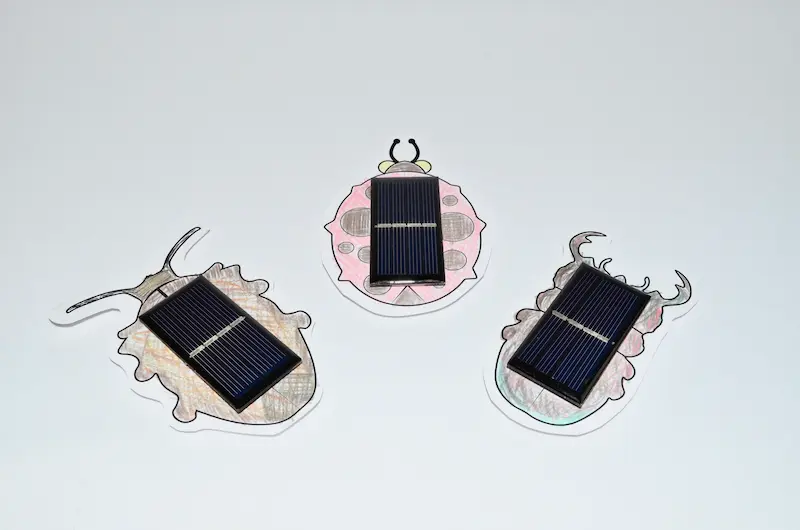 Three solar bugs with colored paper bodies and black solar cells.