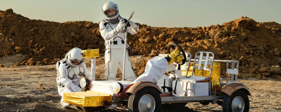 Two astronauts wearing white spacesuits working on a rover vehicle.