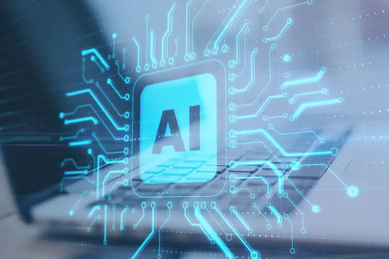 Close-up image of a laptop with a blue holographic overlay of the letters AI on a conceptual computer chip.