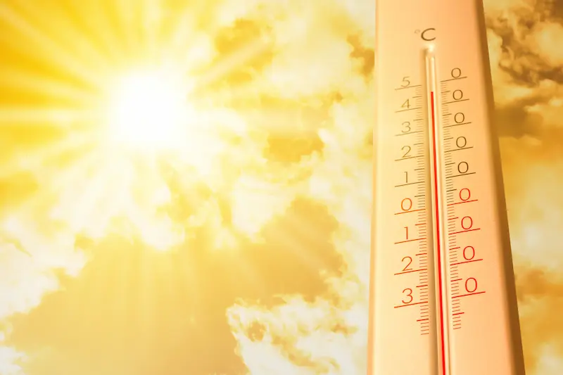A vertical outdoor thermometer showing a high temperature against a sunny background. 