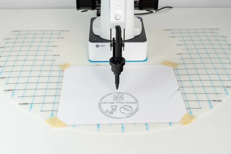 Dobot drawing a circle on a piece of paper. Inside the circle, Dobot has written “Dobot Mars Mission”.