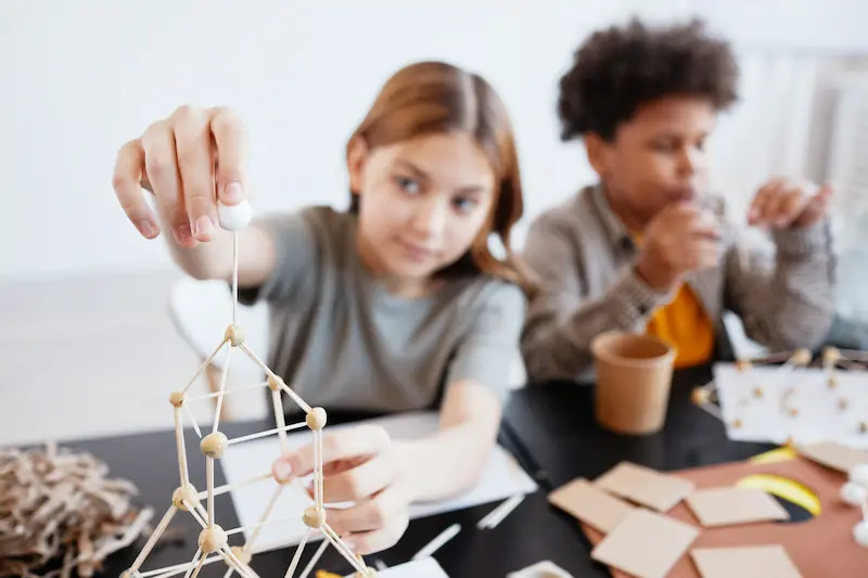 Two children working together on a construction project at a table.