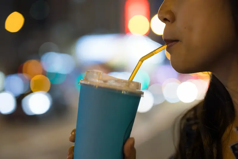 Woman drinking from a paper to-go cup using a straw.