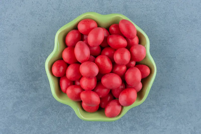 A green bowl filled with small red candies on a grey table.