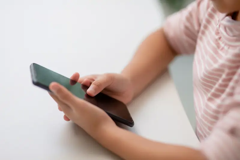Child holding a black smartphone and using the touchscreen on the phone.
