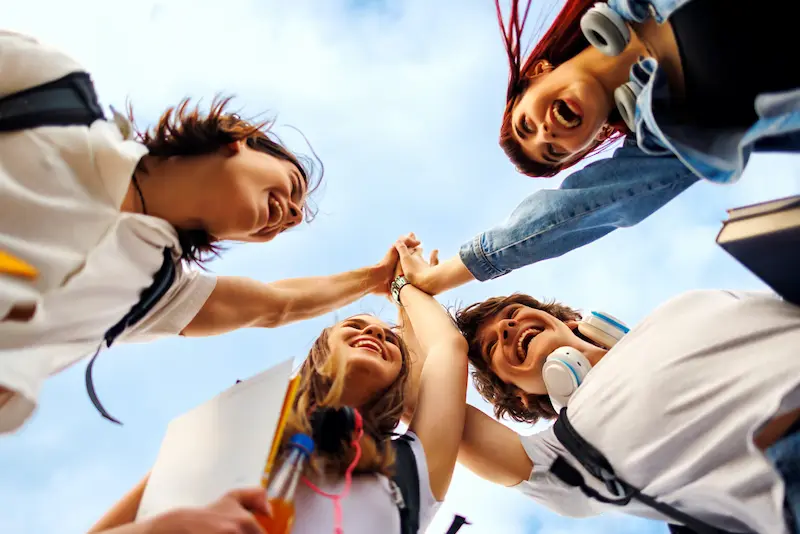 Four smiling students doing a group high five outdoors.
