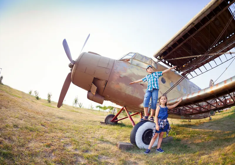 Two children playing on an old airplane in a field.