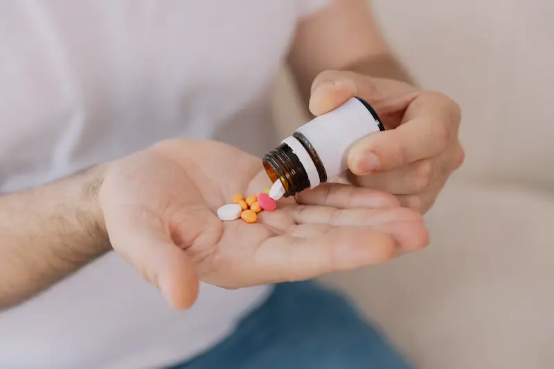 Closeup of a man pouring pills out of a pill container into his hand.
