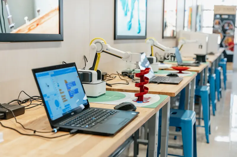 Three Dobot sitting at individual stations, each with a coordinate mat and a laptop.