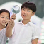 Two children in a science museum. The boy is holding up a magnifying glass.