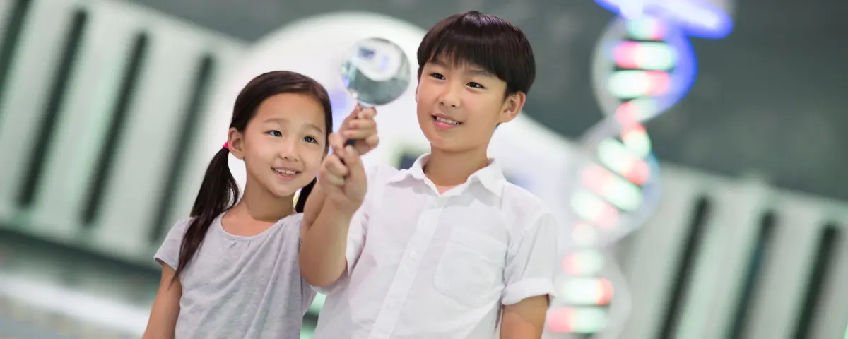Two children in a science museum. The boy is holding up a magnifying glass.