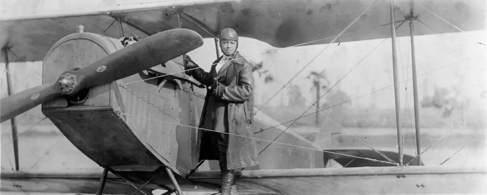Black and white photo of Bessie Coleman in front of her airplane.