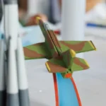 A painted model airplane next to a model rocket ship on a table.
